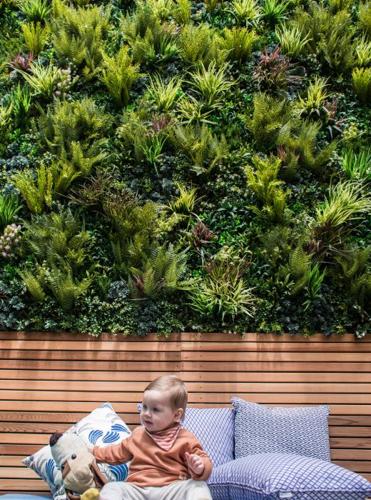 Residential Backyard in front of Vertical Garden and baby playing with toys in front of pillows. 