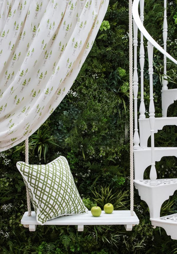 White swing with pillow in front of vertical green wall 