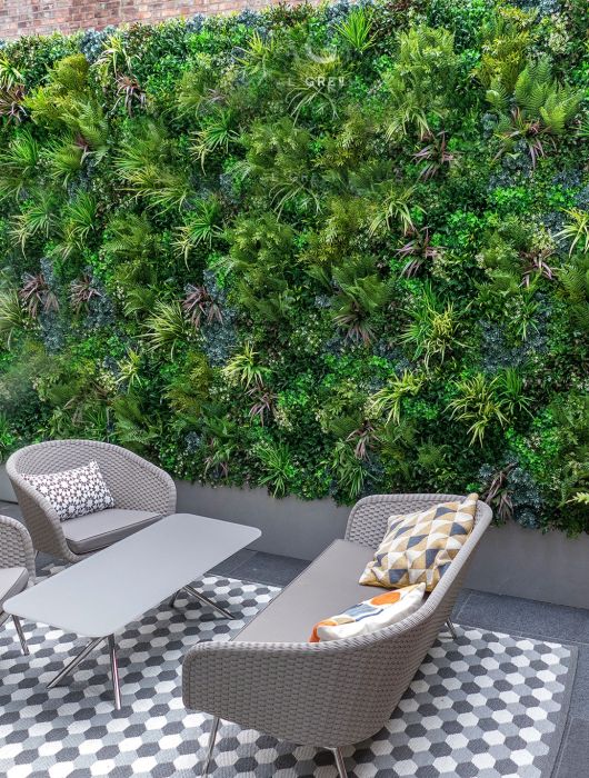 Beautiful Artificial Vertical Garden Green Wall in outdoor backyard area with gray patio furniture over outdoor rug and two vases