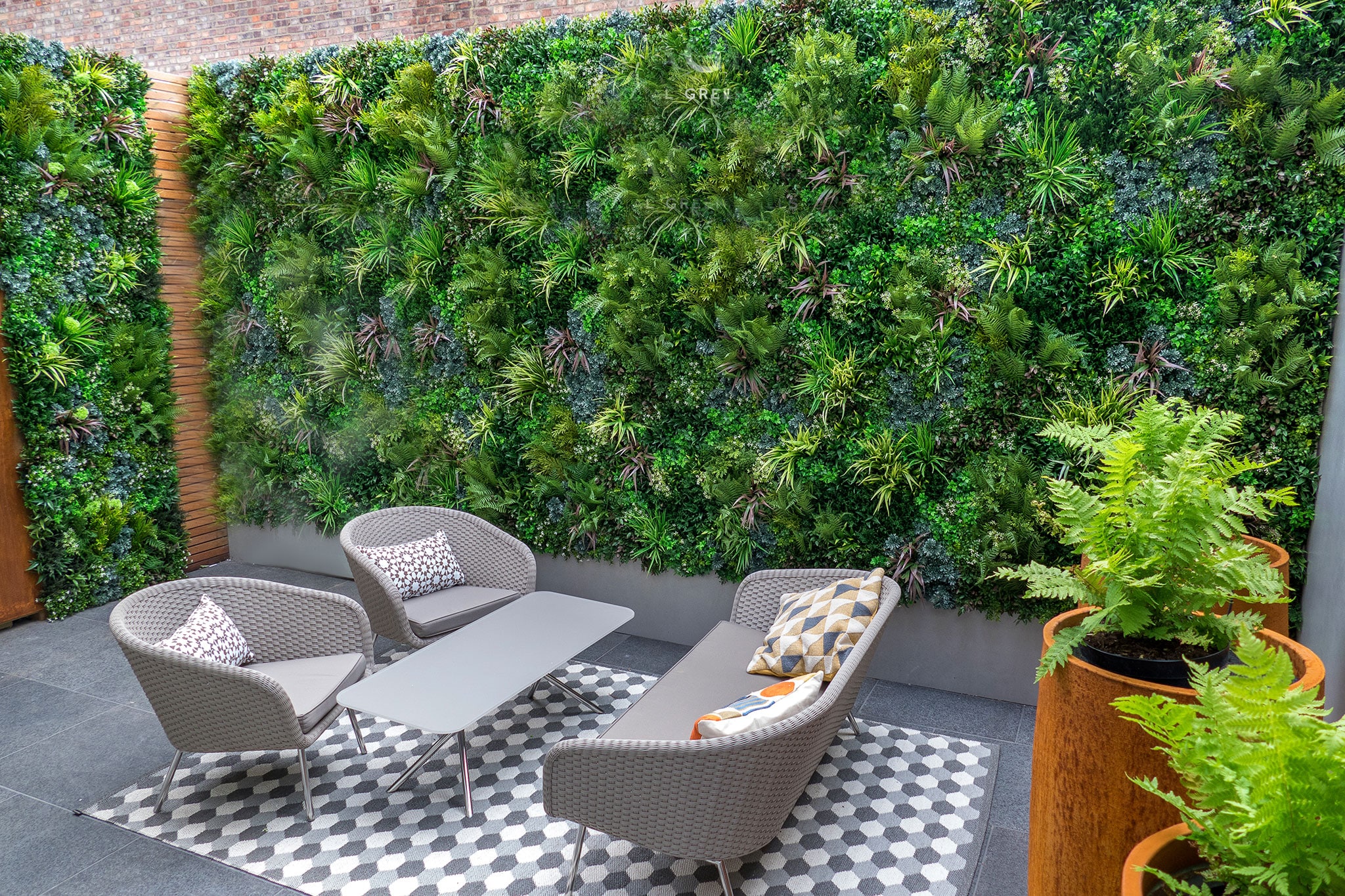 Beautiful Artificial Vertical Garden Green Wall in outdoor backyard area with gray patio furniture over outdoor rug and two vases