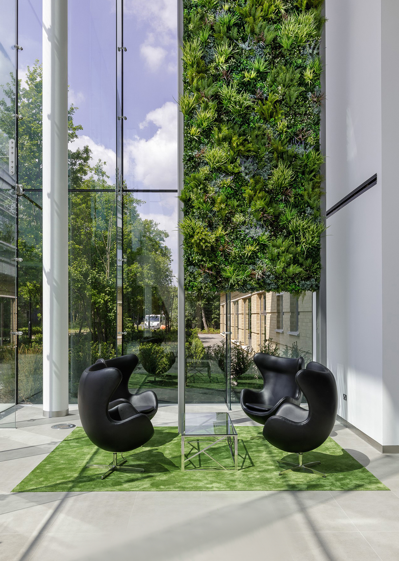 Commercial lobby with beautiful vertical green wall by waiting area with four black chairs